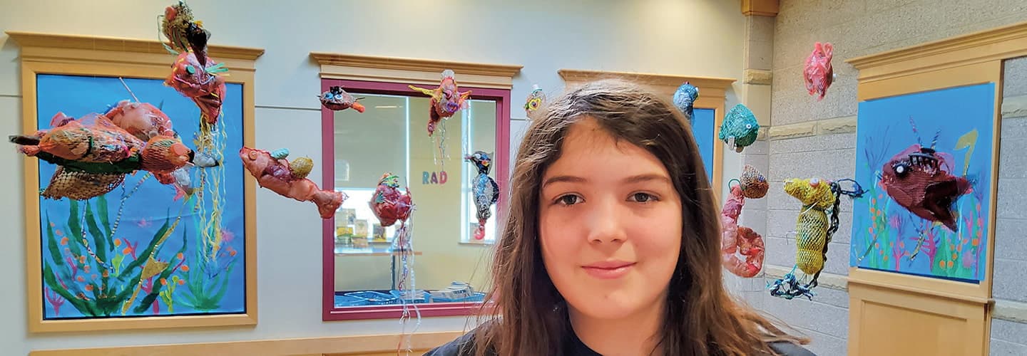 Image of student posing in front of sculptures made from trash